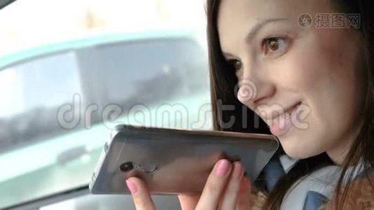 年轻漂亮的女人在坐在车里的手机上说一句语音信息，微笑着。视频