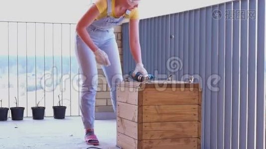 一个女人在露台上做一项非女人的工作-用螺丝刀在木箱里钻一个洞视频