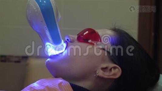 年轻女子在牙科医生办公室用紫外线`机器进行紫外线美白.视频