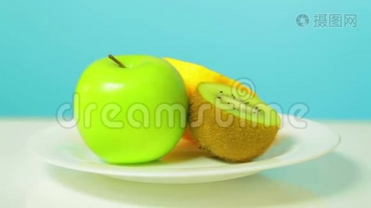 整个绿色的苹果，一半的猕猴桃和橘子放在一个白色的盘子里旋转成一个圆圈视频