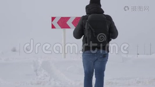 徒步旅行者带着背包，在道路上的冬天选择在两个不同的道路方向之间的道路岔路口。 概念视频