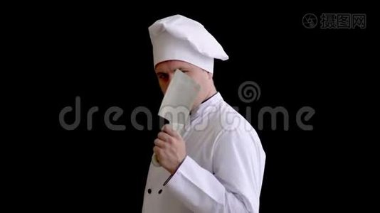 手里拿着厨房斧子的厨师疯子在黑色背景下对镜头凶巴巴地看着。视频