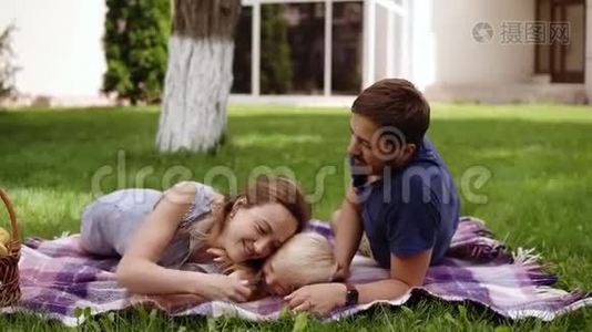 家庭野餐的概念。 年轻的父母躺在草地上，和他的儿子玩。 玩得开心。 头发浓密的孩子爬上去视频