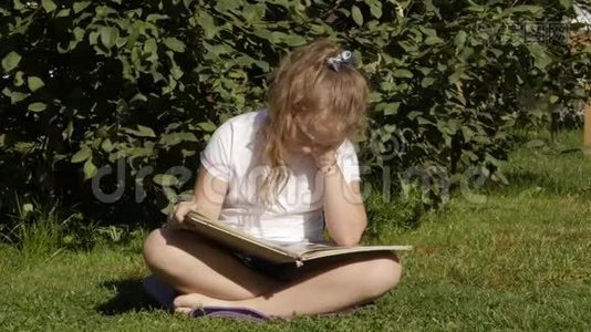 美丽的少女坐在夏天公园的草地上看书。 慢动作视频