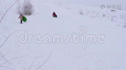 快乐的女孩从大雪中滑出一个充气的雪管。 孩子们在圣诞节假期在公园里玩冬天的游戏视频