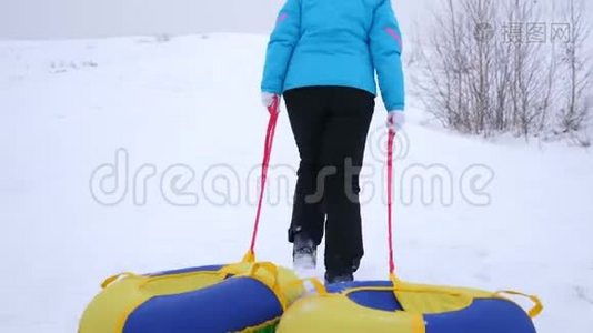 女孩爬上雪山，拉雪橇和一个充气雪管。 在冬季公园休息，过圣诞节视频