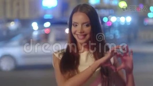夜晚城市里美丽的年轻女子在背景上用模糊的交通灯照相机显示出心脏形状的手指视频