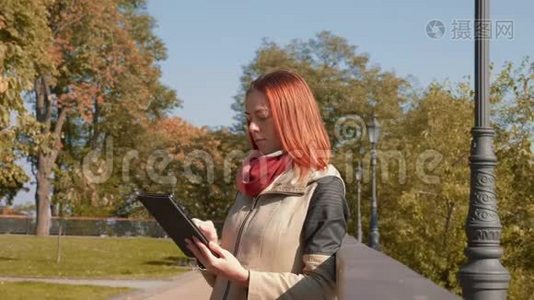 有狐毛的女孩站在户外，在阳光明媚的天气里使用平板电脑，并在网上订购视频