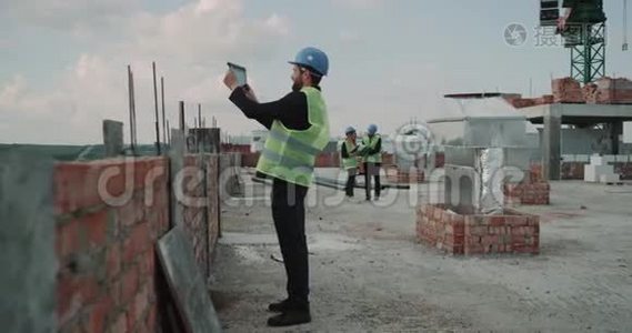 专家工程师在建筑工地屋顶拍照背景两位建筑工人分析视频