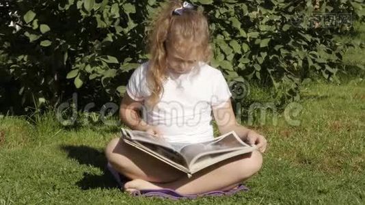 美丽的少女坐在夏天公园的草地上看书。 慢动作视频