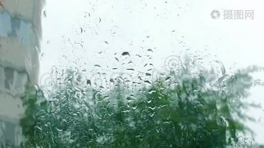 雨滴落在窗户玻璃上，建筑物在背景上。 从窗户看房子，暴风雨天气，强烈视频