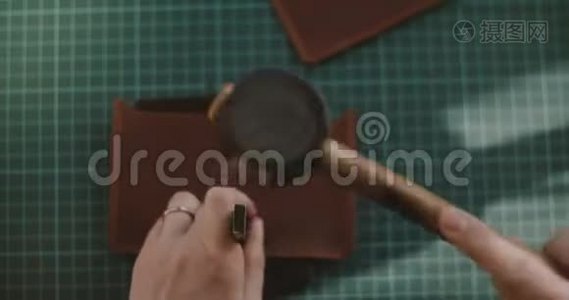 专业女手用锤子和打孔在小块皮革上打洞的特写顶景镜头。视频