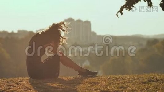 悲伤的女孩剪影独自坐在草地上，如此孤独和哭泣。视频