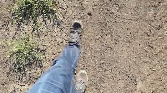 一个穿牛仔裤的人的腿在一条尘土飞扬的道路上缓慢地行走。视频