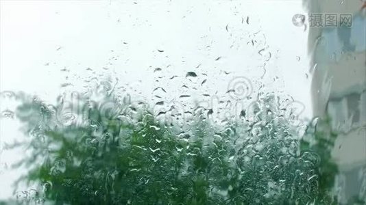 雨滴落在窗户玻璃上，建筑物在背景上。 从窗户看房子，暴风雨天气，强烈视频
