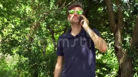 在森林或公园里，有着迷人情感的成熟男人带着胡须和太阳镜，通过智能手机交谈视频