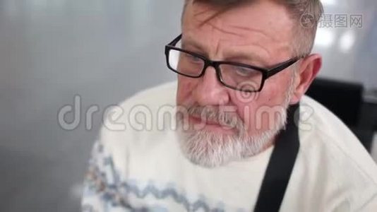 穿着一件白色毛衣的退休旅行者，穿着斯堪的纳维亚风格的毛衣，戴着灰色的胡须和眼镜，坐在等待中视频