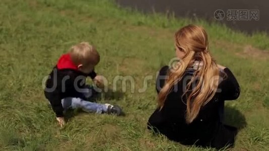 一位快乐的母亲和她的儿子躺在春天河岸上的绿草上。视频