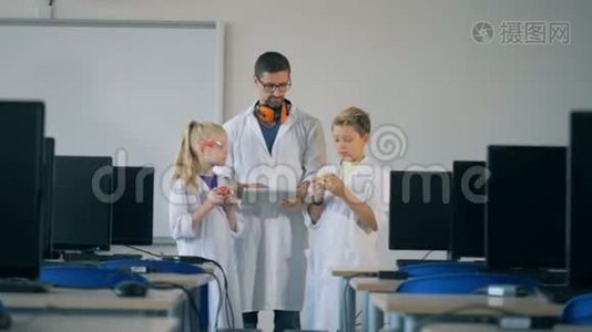 男的实验室工作人员和两个孩子站在电脑室里观察多余的细节视频