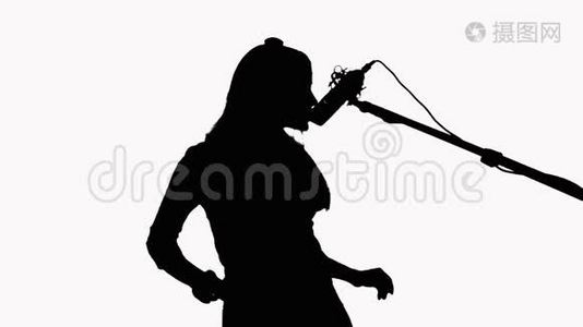 一个长发女孩的剪影，她对着录音棚的麦克风唱歌。在白色背景上。录制音乐视频视频