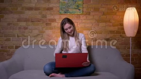 年轻迷人的白种人深色头发的女性特写镜头，她在笔记本电脑上看一部有趣的电影，笑着视频