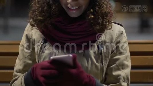 迷人的、快乐的混血女孩带着手套使用智能手机视频