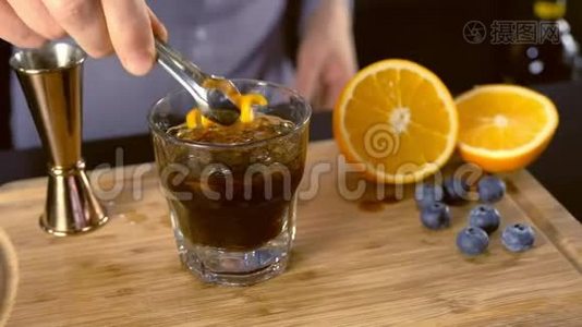 巴曼把橘子和蓝莓放进酒精鸡尾酒里，放在石头玻璃上，用吸管。 双手特写..视频