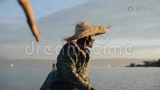 黎明时分，戴着草帽的非洲年轻人坐在摩托艇上，看着海上的帆船。视频