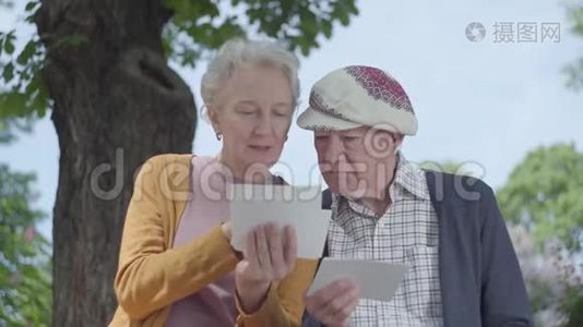 肖像可爱的成熟女人和男人看着老照片，回忆着坐在公园长凳上的快乐时刻视频