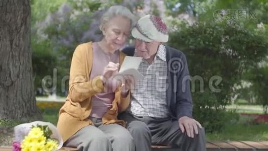 肖像可爱的成年夫妇看着老照片，回忆着坐在公园长凳上的快乐时刻。 成熟成熟视频