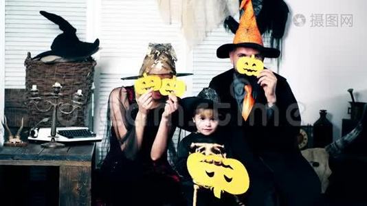 这个男孩，他的父母，穿着女巫、骷髅和女巫的西装，用甜瓜遮住他们的脸。 穿着服装的家人视频