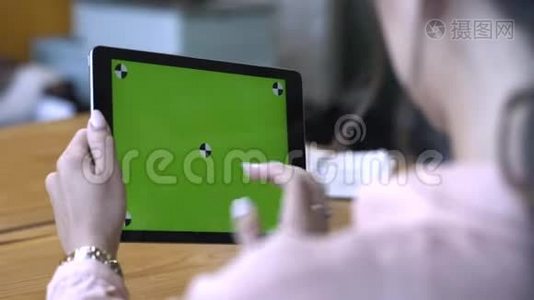 一位棕色头发的年轻女士坐在桌子旁，在彩色钥匙绿色屏幕上滑动着她的平板电脑视频