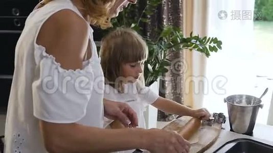 一位美丽的母亲教她的小女儿做饭，在桌子上捏一个面团做饼干。视频