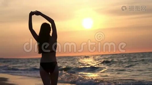 穿黑色泳衣的时髦女孩在日落时进入大海。 我对大海和海滩很满意。 关于视频