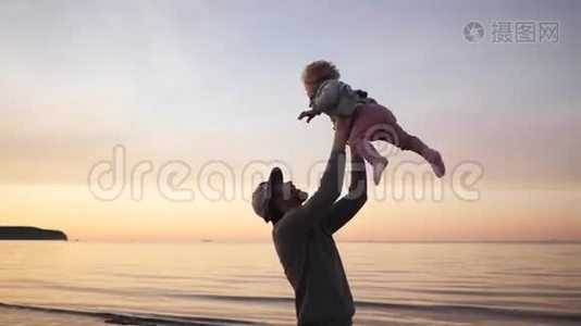 年轻的父亲和小女儿在沙滩上玩耍，拥抱和欢笑，呕吐视频
