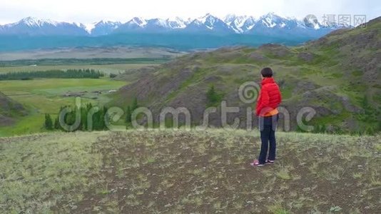 在寒冷的阴天，女徒步旅行者骄傲地站在山顶上。 站在山顶上的女人。 近距离空中飞行视频