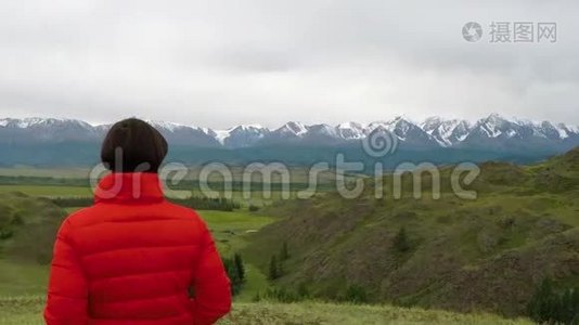 在寒冷的阴天，女徒步旅行者骄傲地站在山顶上。 站在山顶上的女人。 近距离空中飞行视频