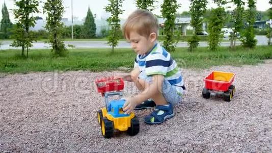 可爱的幼儿男孩在公园操场上玩的4k视频。 男孩在拖车里装砾石视频