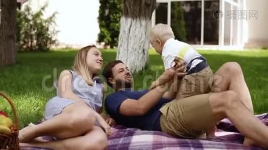 一对年轻夫妇带着一个孩子在公园草地上休息。 三口之家幸福，有一个金发的小男孩视频