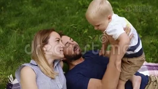 三口之家的高角度镜头。 躺在绿草上，和他的小儿子玩。 快乐生活视频