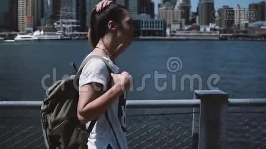 快乐年轻美丽的女孩带着背包走在纽约天际线全景，微笑和享受阳光明媚的早晨。视频