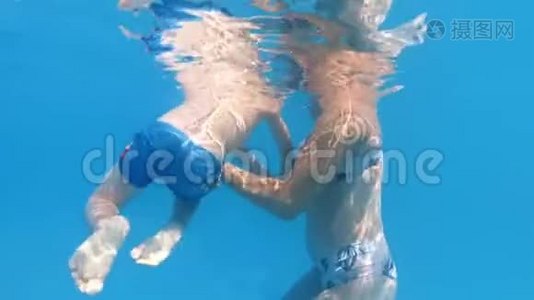 小妈妈在阳光明媚的日子里支持小儿子在游泳池游泳的慢动作水下视频视频