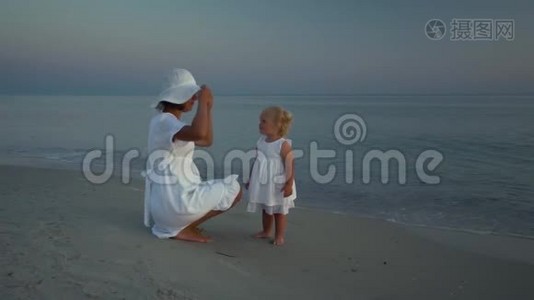 日落时分，年轻漂亮的女人和她的小女儿在海滨散步。 妈妈和她可爱的小女儿试着视频