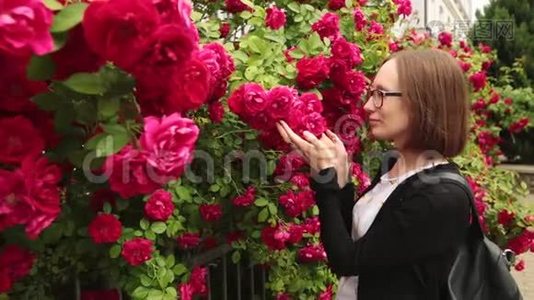 戴眼镜的年轻女人闻着花园里的玫瑰。视频