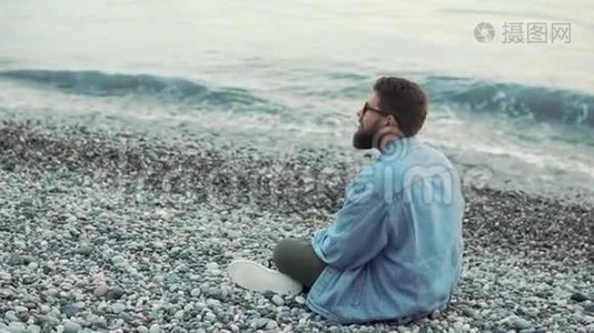 孤独的人坐在海边的沙砾滩上，休息着，转身视频