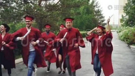 欢快的毕业生在雨中缓慢地奔跑，挥舞着文凭，穿着红色的长袍和迫击炮笑着视频