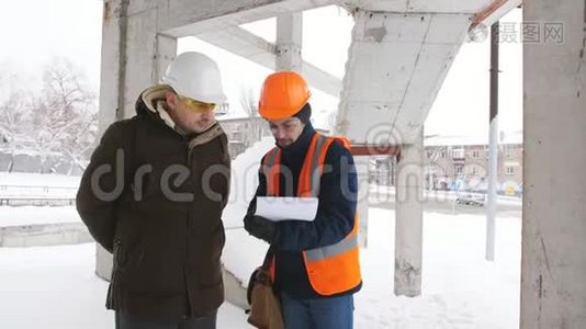 一名工程师和主管讨论冬季在一个下雪的建筑工地上的施工计划。视频