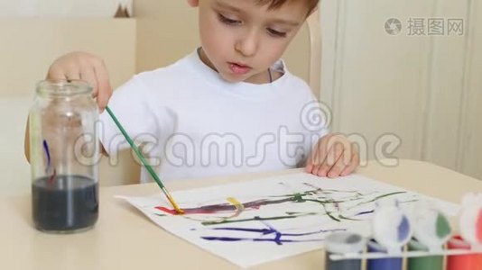 一个孩子`男孩在一张白纸上画水彩画。 一个孩子坐在桌子旁画画。视频