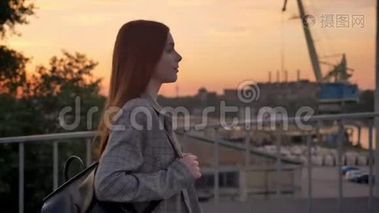 年轻的姜女穿着夹克走过桥，工业工厂背景，日落视频