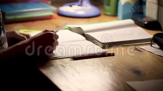 正在学习做家庭作业的男孩少年。 男孩坐在桌子旁，晚上在笔记上写字视频